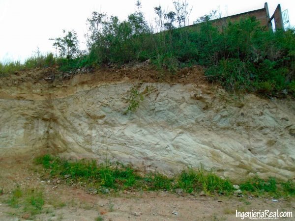 Corte empinado en un talud con material fracturado junto a una construcción