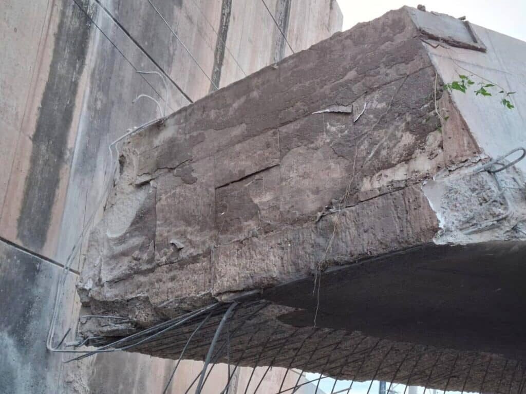Extremo de un tablero de puente de concreto fracturado y desprendido junto al estribo, con acero expuesto y grietas visibles